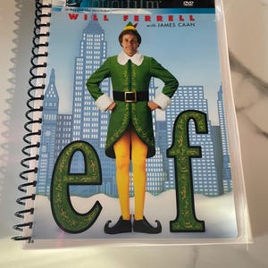May include: A spiral-bound notebook featuring the DVD cover of the movie "Elf." The cover art shows Will Ferrell in a green elf costume with yellow tights, standing in front of a cityscape. The word "Elf" is prominently displayed.