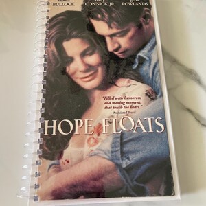 May include: A movie poster for the film "Hope Floats" starring Sandra Bullock, Harry Connick Jr., and Gena Rowlands. The poster features a close-up of Bullock and Connick Jr. embracing. The poster has a white background with black text.