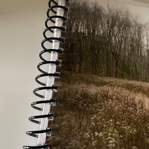 May include: A black spiral bound notebook with a photo of a snowy field and trees in the background.