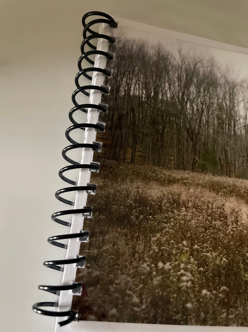 May include: A black spiral bound notebook with a photo of a snowy field and trees in the background.