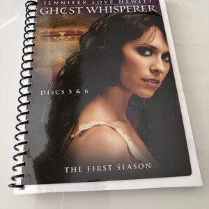 May include: A spiral-bound media case featuring a portrait of Jennifer Love Hewitt on the cover. The text reads Jennifer Love Hewitt Ghost Whisperer Discs 5 & 6 The First Season. The cover art includes a dark background with a small suitcase graphic.