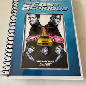 May include: A blue and white notebook with a cover featuring the movie poster for 2 Fast 2 Furious. The poster features Paul Walker, Tyrese Gibson, and Eva Mendes. The text on the poster reads "2 Fast 2 Furious" and "High-Octane Action!"