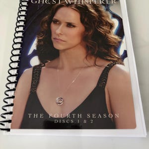 May include: A spiral-bound media case featuring Jennifer Love Hewitt on the cover for Ghost Whisperer The Fourth Season Discs 1 & 2. The cover shows a portrait of the actor wearing a black top and a silver necklace against a dark blue background.