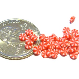 May include: A collection of miniature red and white peppermint candies, each with a pinwheel design, scattered near a U.S. quarter coin. The candies are small, round, and have a classic holiday appearance.
