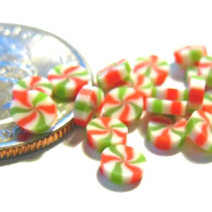 May include: Miniature red, green, and white swirl candies. The candies are arranged on a white surface next to a U.S. quarter for size comparison. The candies have a spiral design.