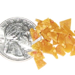 Puede incluir: Una moneda de veinticinco centavos estadounidense junto a un montón de crujiente de cacahuete. Los trozos de crujiente son de color marrón dorado con cacahuetes visibles. La moneda muestra el perfil de George Washington y las palabras "LIBERTY" e "IN GOD WE TRUST".