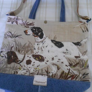 May include: Tote bag with a dog print. The bag features a beige background with a hunting dog design, blue denim bottom, and blue handles. The bag has a floral strap and a tag that says "Pointers".
