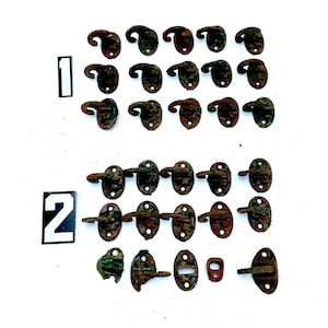 May include: A collection of 24 antique metal hooks and latches in various sizes and shapes. The hooks are rusty and have a green patina. The latches are oval-shaped with a small handle. The hooks and latches are arranged in two rows on a white background. The numbers "1" and "2" are written on the left side of the image.