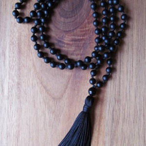 May include: A black beaded necklace with a tassel. The beads are matte and the tassel is made of black thread.