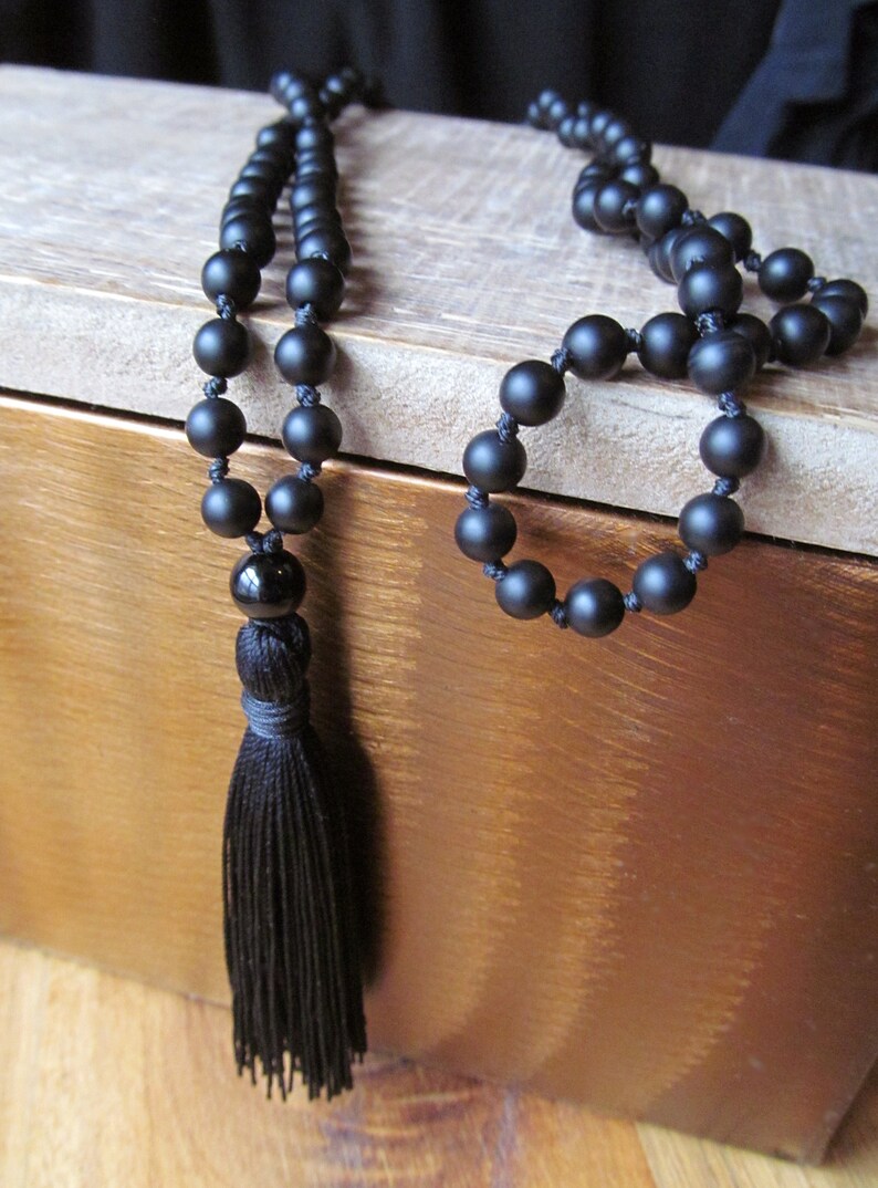May include: A black beaded necklace with a tassel. The necklace is made of matte black beads and has a black tassel at the end.