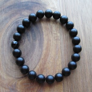 Op de afbeelding: Een zwarte kralen armband met een zwarte onyx edelsteen. De armband is gemaakt van matte zwarte kralen en heeft een eenvoudig ontwerp.