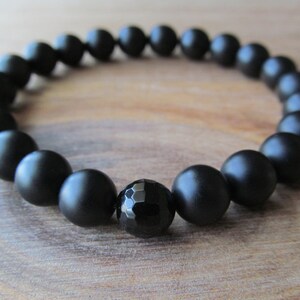 Op de afbeelding: Een zwarte onyx armband met matte zwarte kralen en een gefacetteerde zwarte onyx middelste kraal.