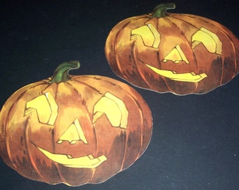 May include: Two orange paper jack-o'-lantern cutouts with yellow painted faces. The jack-o'-lanterns have a toothy grin and triangular eyes.