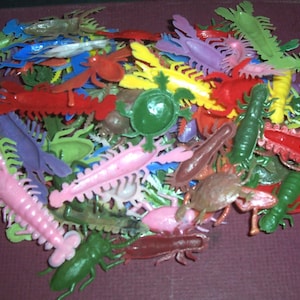 May include: A collection of colorful plastic toy insects, including lobsters, beetles, and centipedes. The toys are in various colors such as red, green, pink, and blue. The toys are scattered together, creating a playful and vibrant display.