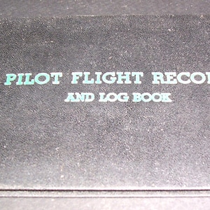 May include: Black leather-bound log book with the title "Pilot Flight Record and Log Book" in white lettering and the name "Bud Cockerell" in white lettering on the side.
