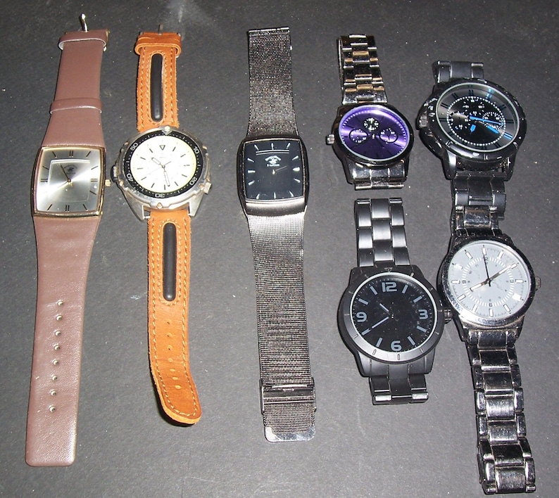 Pode incluir: Uma cole&ccedil;&atilde;o de seis rel&oacute;gios de pulso com designs variados. Est&atilde;o inclu&iacute;dos dois rel&oacute;gios com pulseiras de couro em castanho e bege, um com bracelete de malha escura e tr&ecirc;s rel&oacute;gios de elos met&aacute;licos em prateado, preto e cinzento escuro.