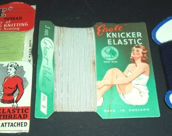 May include: Three spools of thread for sewing and mending. The first spool is labeled "June Elastic Cotton Thread" and is a light green color. The second spool is labeled "Eagle Knicker Elastic" and is white. The third spool is labeled "Olwist Botany Mending Wool" and is dark blue.