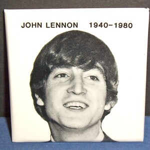May include: Square, white tile featuring a black and white portrait of John Lennon. The text "JOHN LENNON 1940-1980" is printed above the portrait. The image is a close-up shot of the tile.
