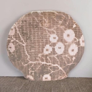 May include: A round, ceramic decorative plate with a unique pattern. The plate features a gray and white floral design with a grid-like texture. The plate has a slightly curved shape and is set against a neutral background.
