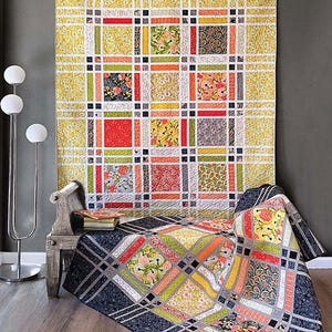 May include: A colorful quilt with a grid pattern, featuring squares of floral and patterned fabrics in shades of red, orange, green, and yellow. The word "FRINGE" is at the top. The quilt is displayed on a bed and wall.