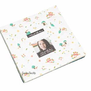 May include: A Moda Fabrics charm pack featuring a white background with a repeating pattern of small flowers, leaves, and mushrooms in shades of pink, green, and blue. The pack includes 42 - 2.5 inch squares. The text "Moda Fabrics" and "Sunshine Pie Co." are visible on the fabric.