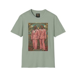 May include: A sage green short-sleeve t-shirt featuring a central graphic print of two individuals in pink suits standing before an ornate archway. The text "CLIPSE" appears at the top of the graphic, and "STATION 73" is printed at the bottom.