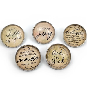 Op de afbeelding: Vijf ronde knopen met zilveren randen, elk met inspirerende citaten en bijbelverzen. De knopen tonen zinnen als "I am a child of God" en "I choose joy" op een vintage-achtige achtergrond.