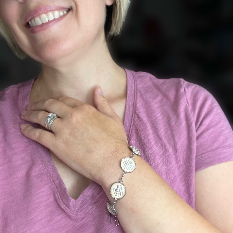May include: A silver charm bracelet with multiple round charms featuring inspirational quotes. The charms are connected by a silver chain. The bracelet is worn on a person's wrist.