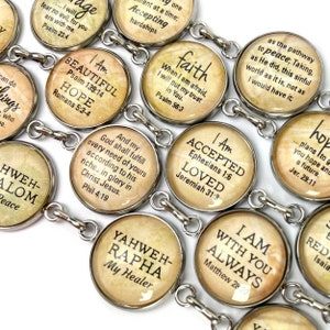 May include: A silver charm bracelet with round, silver-toned charms featuring inspirational quotes and bible verses. The charms have a vintage, aged look with a beige background and black text. Some of the quotes include "I Am Beautiful", "Hope", "Faith", "Accepted", "Loved", "Yahweh-Rapha My Healer", "I Am With You Always", and "...plans to give you hope and a future".