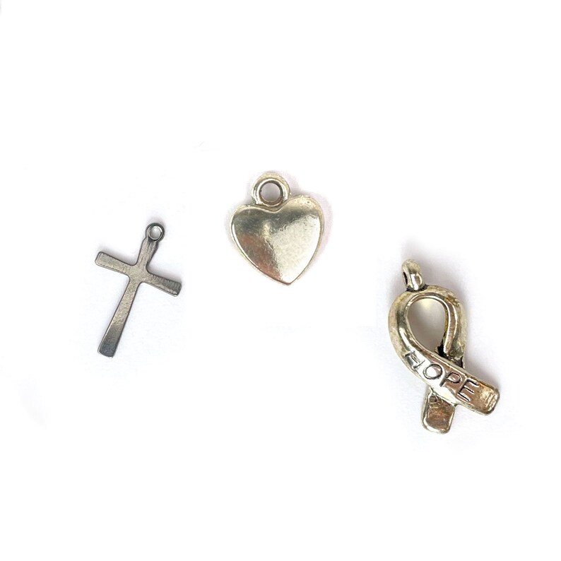 May include: Three silver charms: a cross, a heart, and a ribbon with the word "HOPE" inscribed on it.
