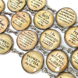 May include: A silver charm bracelet with round, silver-toned charms featuring inspirational quotes and bible verses. The charms have a vintage, aged look with a beige background and black text. Some of the quotes include "I Am Beautiful", "Hope", "Faith", "Accepted", "Loved", "Yahweh-Rapha My Healer", "I Am With You Always", and "...plans to give you hope and a future".