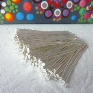 May include: A close-up of a bundle of silver-coloured head pins. The pins are arranged in a fan shape and are all the same size. The pins are sharp and pointed at one end and have a round head at the other end.