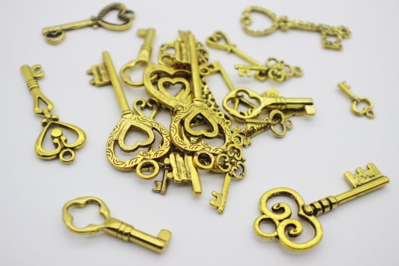 May include: A pile of antique gold-toned skeleton keys with ornate heart-shaped keyholes. The keys are scattered on a white surface.