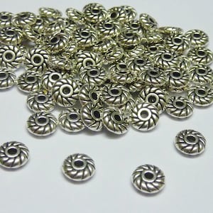May include: A pile of silver metal beads with a decorative design. The beads are round with a hole in the centre.