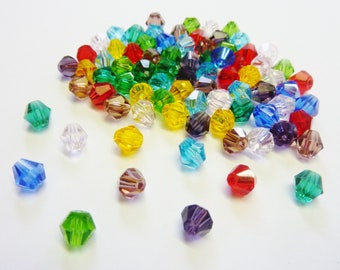 May include: A large assortment of colorful faceted glass beads in various shades of red, green, blue, yellow, and purple. The beads are scattered on a white surface.