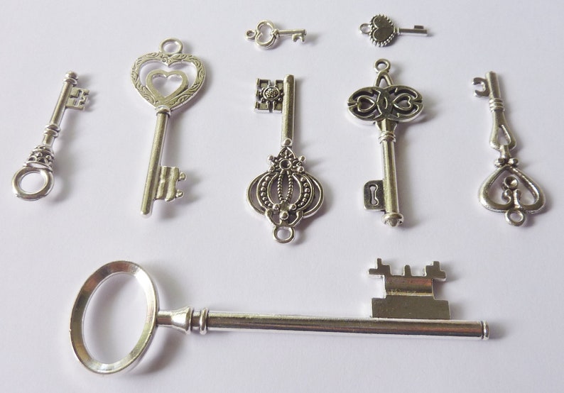 May include: Assortment of eight silver-toned skeleton keys with ornate designs. The keys are arranged on a white surface.