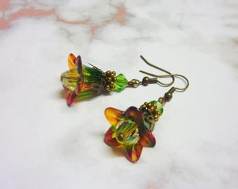 May include: A pair of floral-shaped earrings with a bronze-colored hook. The earrings feature colorful, faceted beads in shades of orange, yellow, green, and red, arranged to resemble flowers. Small gold-colored beads accent the design.
