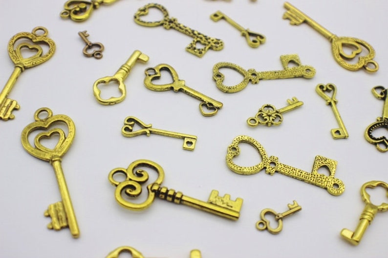 May include: A collection of antique gold-toned skeleton keys with ornate designs. The keys are scattered on a white surface.