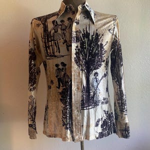 May include: A vintage button-down shirt with a cream-colored background and a black and white illustration pattern. The long-sleeved shirt features a collared neckline and a series of buttons down the front. The illustration depicts figures in a park setting.