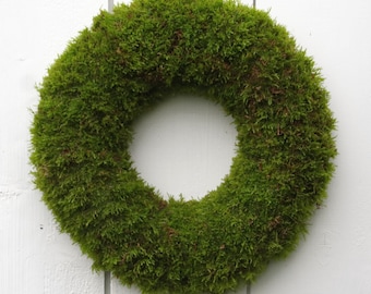 May include: A green moss wreath hanging on a white wooden wall.