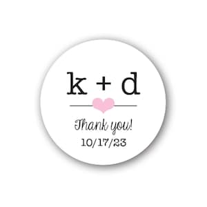 Puede incluir: Una pegatina redonda blanca con texto negro y un corazón rosa. El texto dice "k + d" encima de una línea, con "Thank you!" y la fecha "10/17/23" debajo. Ideal para bodas o eventos especiales.