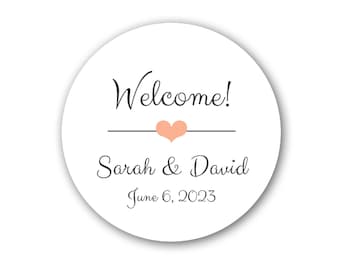 May include: A white round sticker with black text that says "Welcome!" with a small peach heart above the text. Below the heart is the text "Sarah & David" and the date "June 6, 2023".