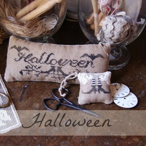 Könnte beinhalten: Zwei kleine bestickte Kissenbezüge mit Halloween-Motiv. Der größere Kissenbezug trägt die Aufschrift "Halloween" mit einer schwarzen Katze und Fledermäusen. Der kleinere Kissenbezug hat einen Hexenstiefel und einen weißen Spitzenkragen. Die Kissen liegen auf einem Holztisch mit anderen Dekorationsartikeln.