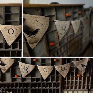 May include: A Halloween banner with the word "BOO" spelled out on triangular fabric flags. The flags are decorated with black crows and a handwritten script. The banner is hanging from a wooden frame.