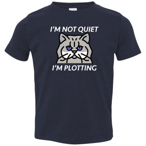 Pode incluir: Uma camiseta azul marinho para crian&ccedil;as pequenas com uma ilustra&ccedil;&atilde;o de um gato branco e o texto "N&atilde;o estou quieto, estou tramando".