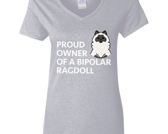 Pode incluir: Camiseta cinza claro com decote em V com o texto branco "PROUD OWNER OF A BIPOLAR RAGDOLL". Uma ilustração de desenho animado de um gato Ragdoll está à direita do texto. O gato é branco com marcas pretas.