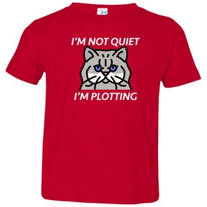 Pode incluir: Camiseta vermelha para crian&ccedil;a pequena com uma ilustra&ccedil;&atilde;o de um gato branco e o texto "N&atilde;o estou quieto, estou a tramar".