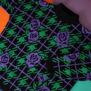 May include: A black sweater with a green and purple plaid pattern and purple roses.