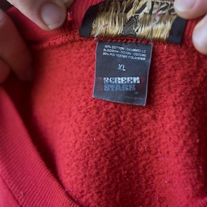 Może przedstawiać: Czerwona bluza z metką Screen Stars. Metka zawiera napis "50% bawełna, 50% poliester" i "XL".