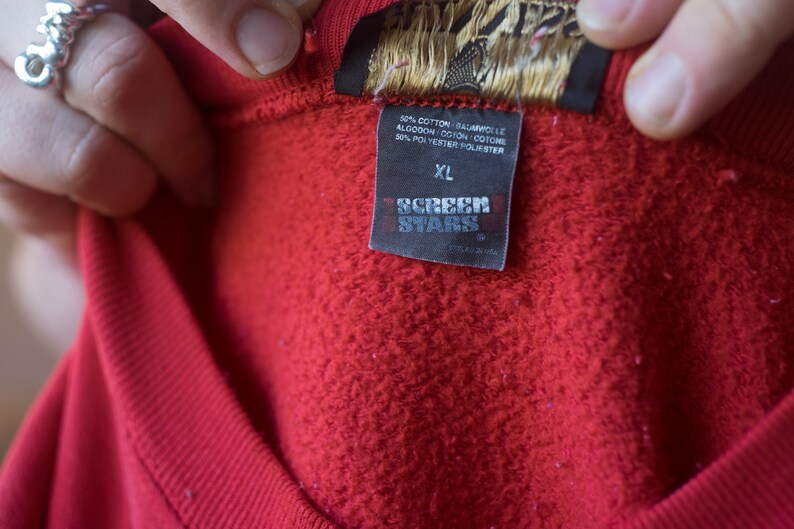 Może przedstawiać: Czerwona bluza z metką Screen Stars. Metka zawiera napis "50% bawełna, 50% poliester" i "XL".